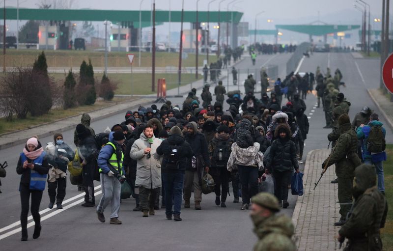 &copy; Reuters. 　ポーランドの治安維持部隊は１６日、ベラルーシとの国境で投石する移民に対し放水を行った。写真は国境付近の物流センターに向かう移民と監視するベラルーシ兵。提供写真（２０２１