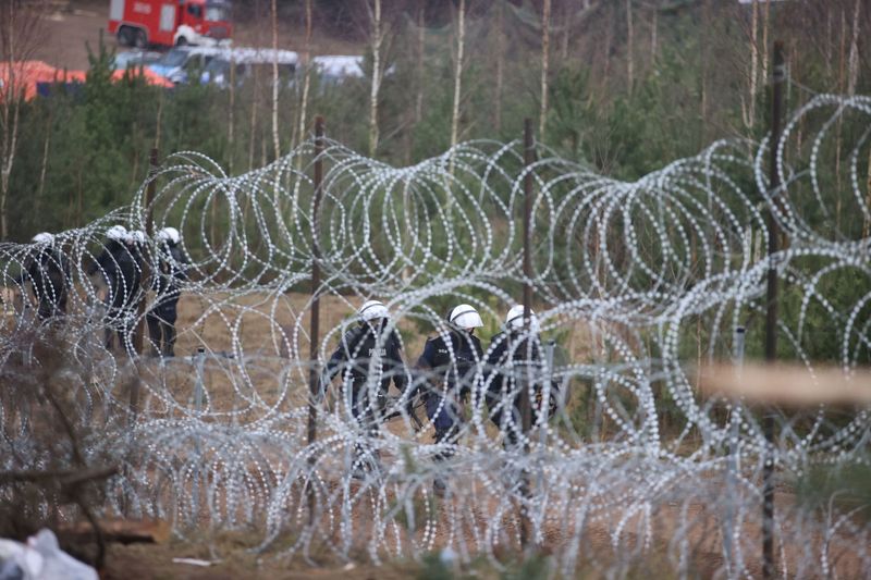 &copy; Reuters. A view from an empty migrants' camp shows Polish law enforcement officers, who walk along a fence on the Belarusian-Polish border in the Grodno region, Belarus November 18, 2021.  Leonid Scheglov/BelTA/Handout via REUTERS  ATTENTION EDITORS - THIS IMAGE H