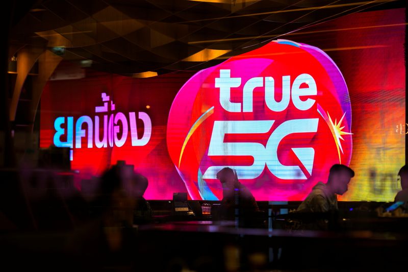 © Reuters. People are silhouetted in front of an electronic screen showing logo of the True Corp. at a department store in Bangkok, Thailand, November 22, 2021. REUTERS/Athit Perawongmetha