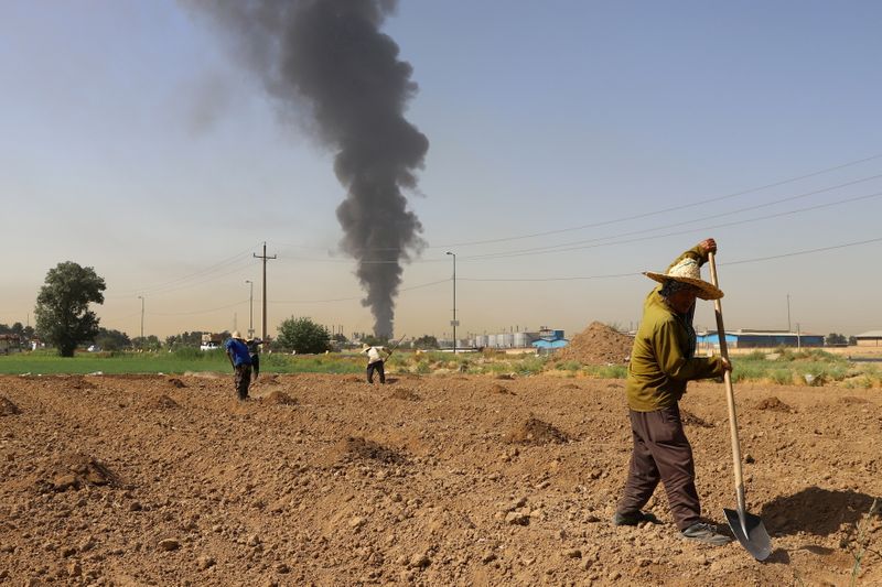 &copy; Reuters. مزارعون يعملون في حقل وفي الخلفية دخان يتصاعد من مصفاة للنفط في العاصمة الإيرانية طهران يوم 3 يونيو حزيران 2021.
(صورة لرويترز من وكالة أنباء غ