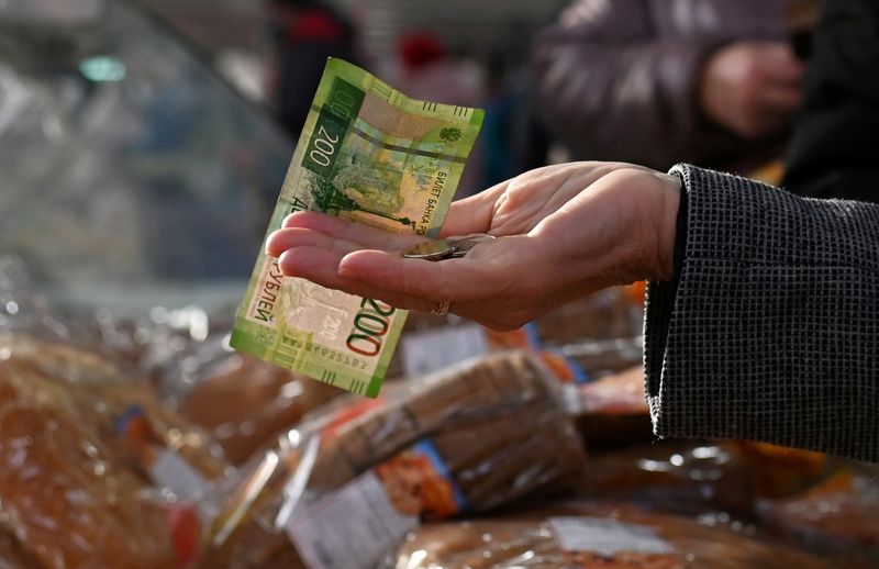 © Reuters. FILE PHOTO: A customer hands over Russian rouble banknotes and coins to a vendor at a market in Omsk, Russia October 29, 2021. REUTERS/Alexey Malgavko/File Photo