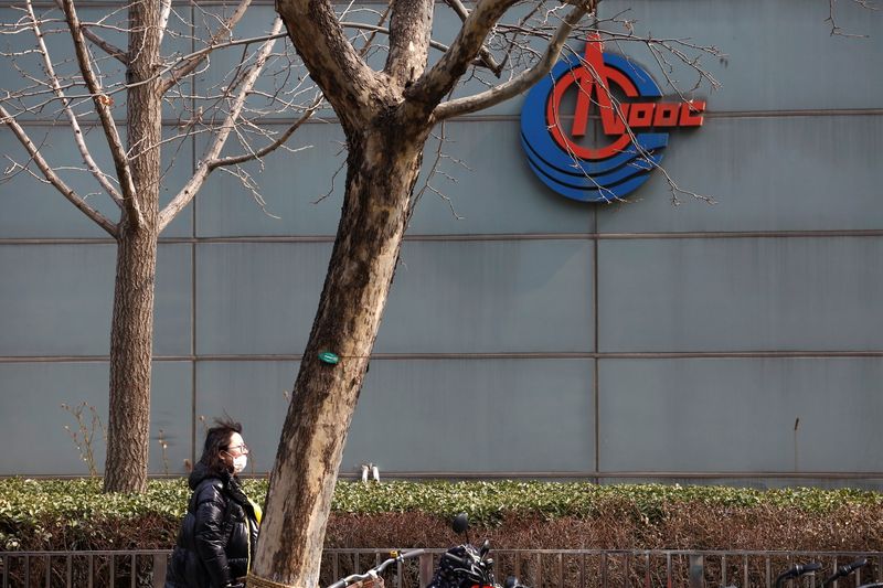 &copy; Reuters. A woman wearing a face mask walks past a sign of China National Offshore Oil Corp (CNOOC) outside its headquarters in Beijing, China March 8, 2021. REUTERS/Tingshu Wang