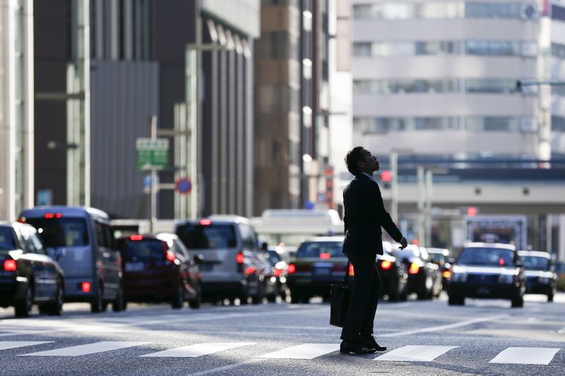 &copy; Reuters. FILE PHOTO: A businessman looks up as he crosses a street in a business district in central Tokyo, Japan, December 8, 2015. Japan's economy dodged recession in the third quarter with the initial estimate of a contraction revised to an annualised expansion