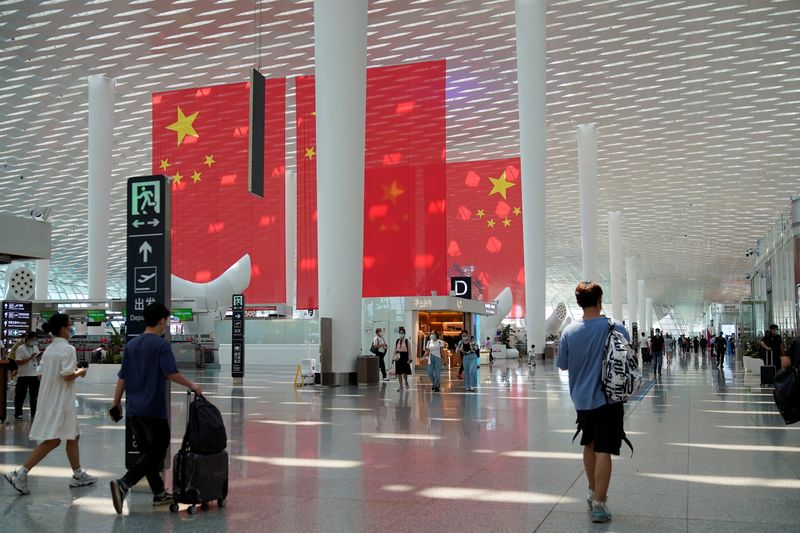 &copy; Reuters. FILE PHOTO: Travellers walk past Chinese flags ahead of China's National Day and Golden Week holiday, at Shenzhen Baoan International Airport in Shenzhen, Guangdong province, China September 30, 2021. REUTERS/Aly Song
