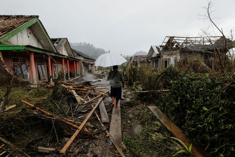 &copy; Reuters. A man with an umbrella walks amongst damaged houses looking for his goat in an area affected by the eruption of Mount Semeru volcano in Curah Kobokan, Pronojiwo district, Lumajang, Indonesia, December 6, 2021. REUTERS/Willy Kurniawan  