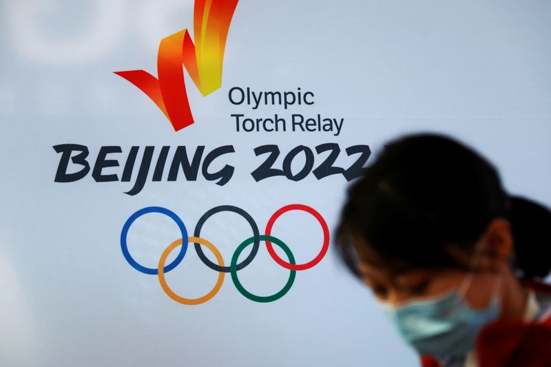 &copy; Reuters. A woman wearing a face mask stands in front of the logo of the Beijing 2022 Winter Olympics before the Olympics flame exhibition tour at Beijing University of Posts and Telecommunications, in Beijing, China December 9, 2021. REUTERS/Carlos Garcia Rawlins