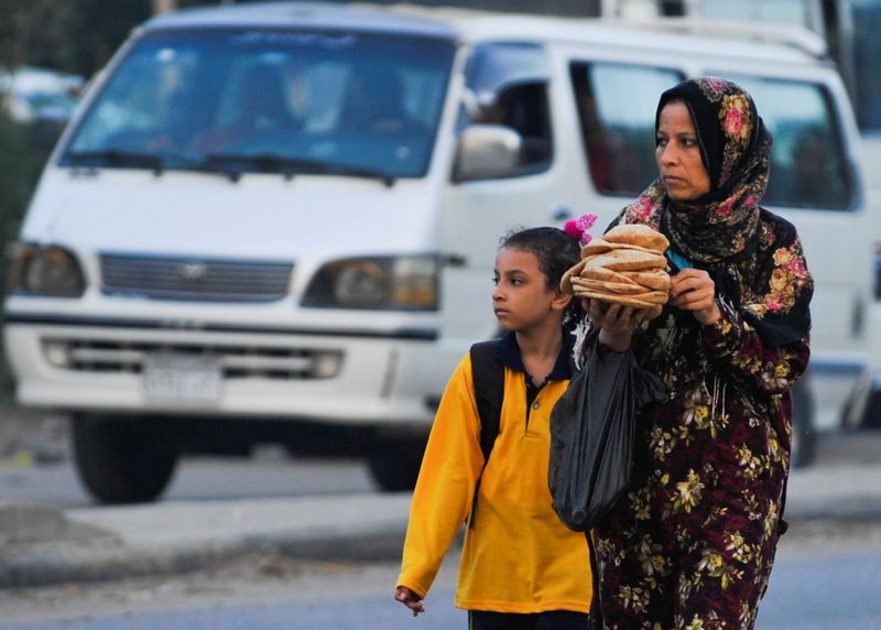 © Reuters. مصرية تحمل الخبز وهي توصل ابنتها للمدرسة في ضاحية أوسيم بمحافظة الجيزة في العاشر من أكتوبر تشرين الأول 2021. تصوير شكري حسين- رويترز.