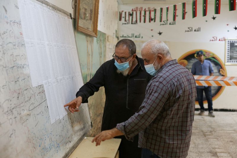 © Reuters. شخصان يبحثان عن اسميهما في الكشوف الانتخابية في طرابلس يوم 8 نوفمبر تشرين الثاني 2021. تصوير: حازم أحمد-رويترز.