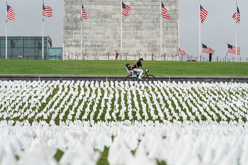 © Reuters. FILE PHOTO: A cyclist rides past an exhibition of white flags representing Americans who have died of coronavirus disease (COVID-19), placed over 20 acres of the National Mall, in Washington, U.S., September 17, 2021. REUTERS/Joshua Roberts