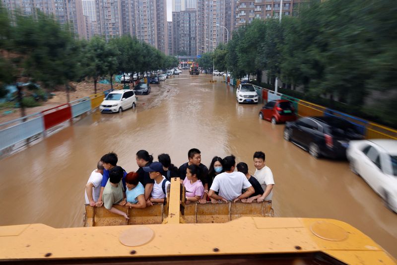 &copy; Reuters. FILE PHOTO: People ride on a front loader as they make their way through a flooded road following heavy rainfall in Zhengzhou, Henan province, China July 23, 2021. REUTERS/Aly Song