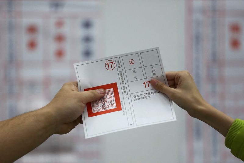 &copy; Reuters. عاملان في مركز اقتراع يظهران ورقة تصويت في استفتاء جرى بتايبه يوم السبت. تصوير:رويترز.
