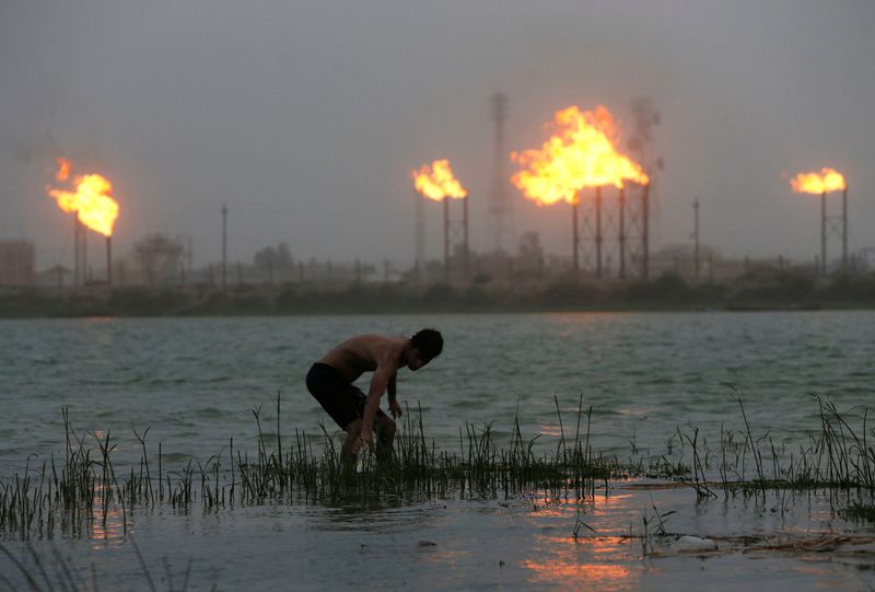 &copy; Reuters. FILE PHOTO: Man stands in Shatt al-Arab River with flames rising from oil refinery pipes in the background in Basra, Iraq July 23, 2020. picture taken July 23, 2020. REUTERS/Essam al-Sudani