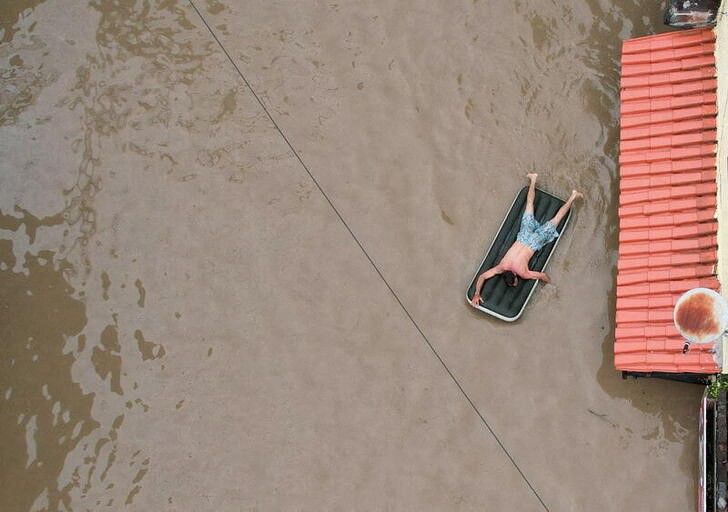 &copy; Reuters. Un hombre utiliza un colchón inflable en medio de una inundación causada por el desborde del río Cachoeira en Itabuna, estado de Bahía, Brasil, Diciembre 26, 2021. Fotografía tomada con un dron. REUTERS/Leonardo Benassatto  NO REVENTAS. NO ARCHIVOS
