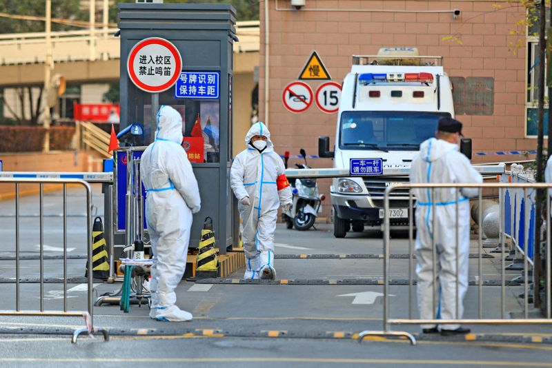 © Reuters. FILE PHOTO: Workers in protective suits stand at an entrance to a university's residential area under lockdown following the coronavirus disease (COVID-19) outbreak in Xian, Shaanxi province, China December 20, 2021. China Daily via REUTERS/File Photo