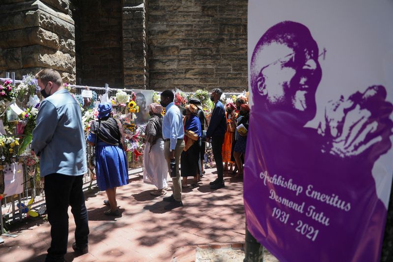 &copy; Reuters. Miembros de la familia del fallecido arzobispo Desmond Tutu caminan frente a una ofrenda de flores y mensajes de condolencia dejandos por miembros del público, afuera de la Catedral St. Georges, en Ciudad del Cabo, Sudáfrica. 31 de diciembre, 2021. REUT