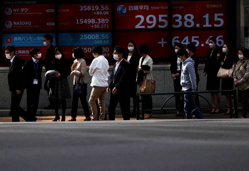 &copy; Reuters. FILE PHOTO: Passersby wearing protective face masks are seen in front of an electronic board showing Japan’s Nikkei share average, amid the coronavirus disease (COVID-19) pandemic, in Tokyo, Japan November 1, 2021. REUTERS/Issei Kato