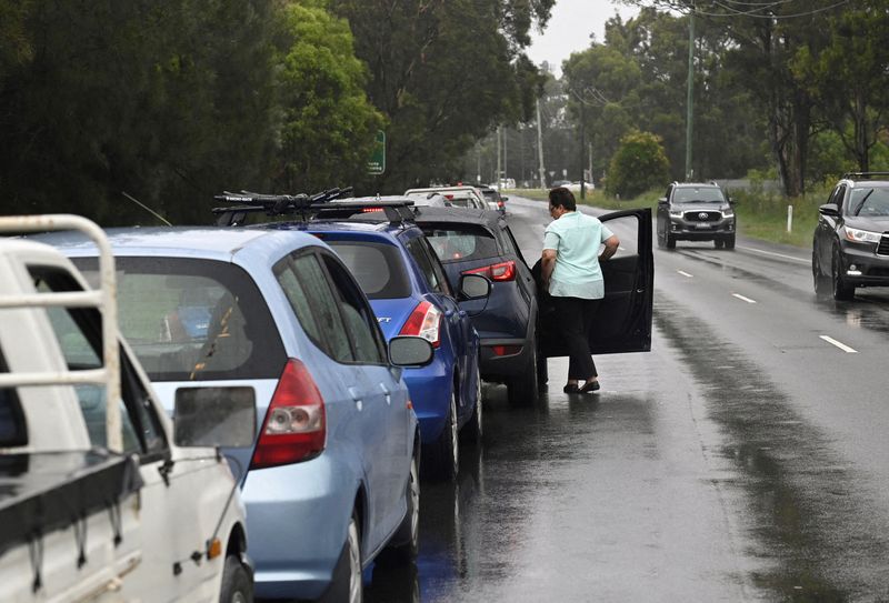 © Reuters. A woman in line at a coronavirus (COVID-19) testing centre steps out of her vehicle to look at the queue of traffic blocking a Western Sydney highway in Sydney, Australia, January 5, 2022.  REUTERS/Jaimi Joy 
