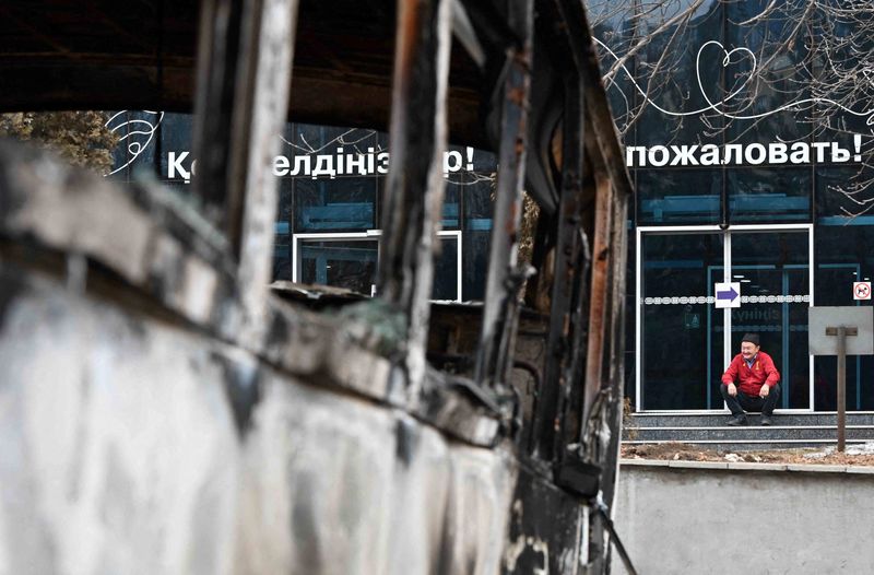&copy; Reuters. Un hombre se sienta en las escaleras de un edificio mientras un vehículo, que fue quemado durante las protestas masivas provocadas por el aumento del precio del combustible, se ve en primer plano, en Almaty, Kazajistán 9 de enero de 2022. REUTERS/Mariya