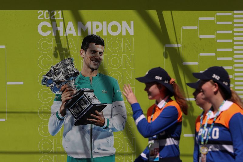 &copy; Reuters. Los recogepelotas pasan por delante de una imagen del tenista serbio Novak Djokovic mientras siguen las dudas sobre la batalla legal en torno a su visado para jugar en el Open de Australia, en Melbourne Park en Melbourne, Australia, 12 de enero de 2022. R