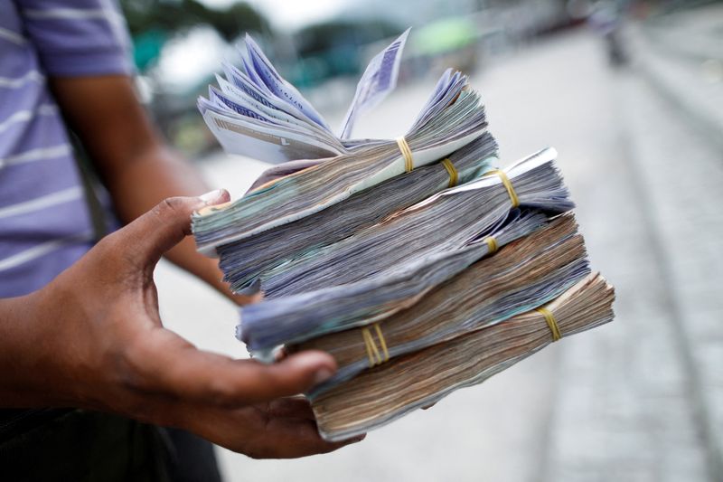 &copy; Reuters. FILE PHOTO: The assistant of a bus driver holds Bolivar banknotes, worth between 0.01 and 0.25 US Dollars, after Venezuela's central bank announced it will cut six zeros from prices, in Caracas, Venezuela August 5, 2021. REUTERS/Leonardo Fernandez Viloria