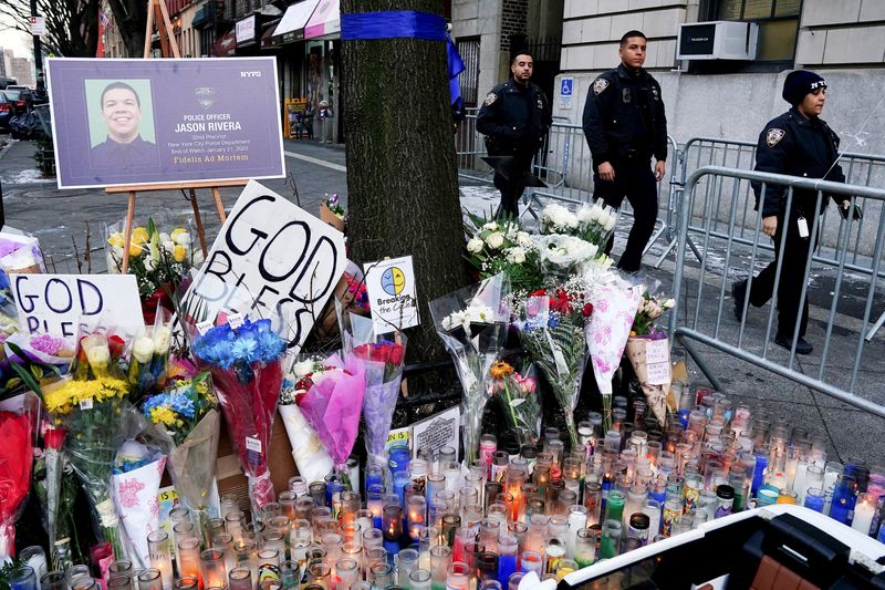 © Reuters. FILE PHOTO: Police officers walk past a makeshift memorial at the 32nd Precinct after the death of officer Jason Rivera, who was shot while responding to a domestic violence call, in the Harlem neighborhood, of New York City, U.S., January 24, 2022.  REUTERS/Carlo Allegri/File Photo