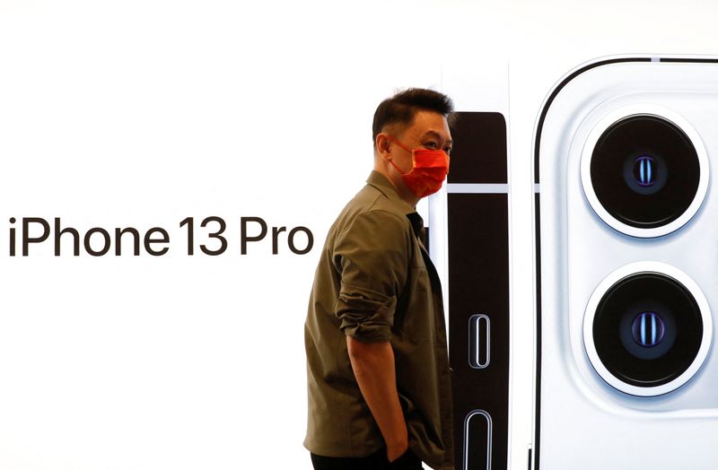 &copy; Reuters. Un hombre con una mascarilla camina frente a la imagen de un teléfono iPhone 13 Pro en una Apple Store en el día del lanzamiento a la venta de la nueva serie iPhone 13 de Apple en Pekín, China. 24 de septiembre, 2021. REUTERS/Carlos Garcia Rawlins
