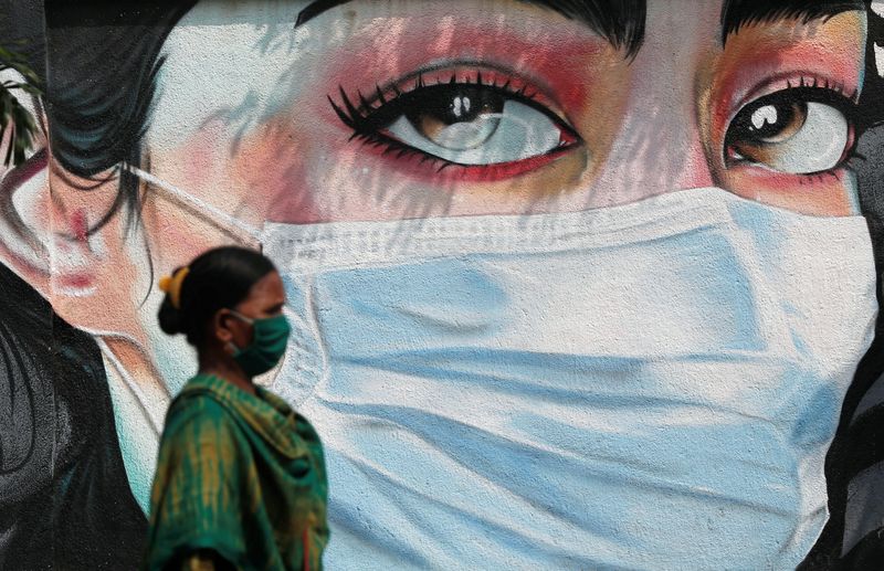 &copy; Reuters. امرأة تمر أمام رسم جرافيتي لفتاة تضع كمامة في مومباي بالهند - صورة من أرشيف رويترز 