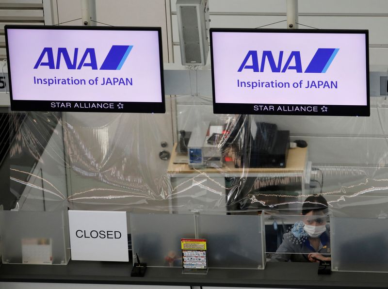 &copy; Reuters. FILE PHOTO: A staff member of All Nippon Airways (ANA) wearing a protective face mask sits behind a plastic curtain, installed in order to prevent infections following the coronavirus disease (COVID-19) outbreak, at a counter in a terminal of the Tokyo In