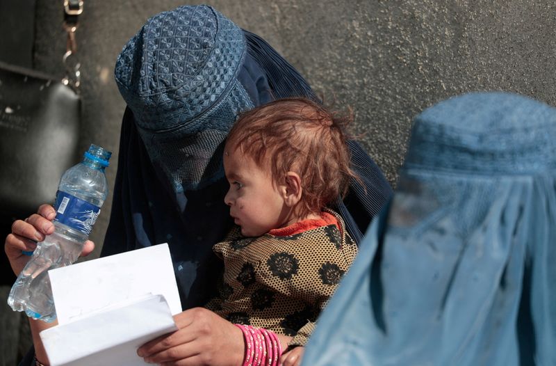 © Reuters. FILE PHOTO: A displaced Afghan woman holds her child as she waits with other women to receive aid supply outside an UNCHR distribution center on the outskirts of Kabul, Afghanistan October 28, 2021. REUTERS/Zohra Bensemra