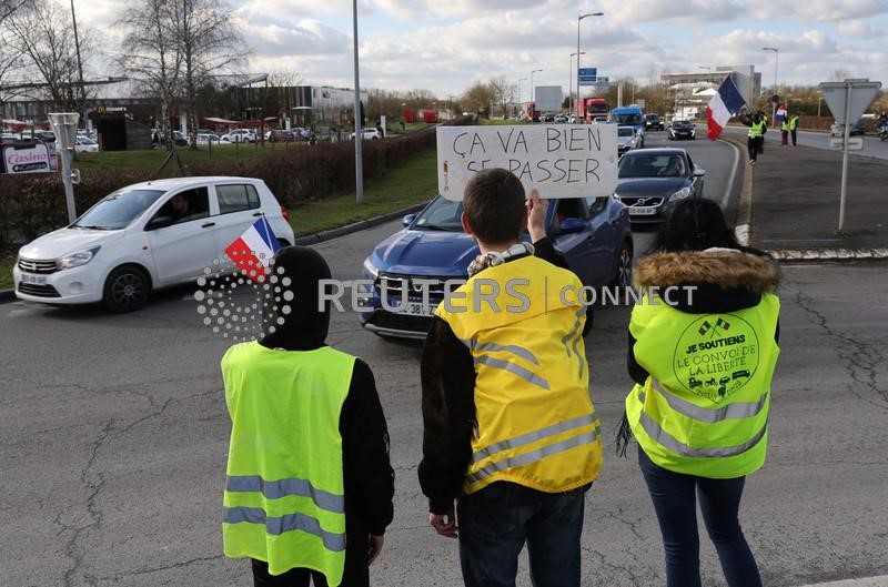 © Reuters. Partidarios y miembros del movimiento de los chalecos amarillos sostienen pancartas en un estacionamiento de un centro comercial en Longueau mientras animan a los conductores de automóviles franceses contra las restricciones de COVID durante su 