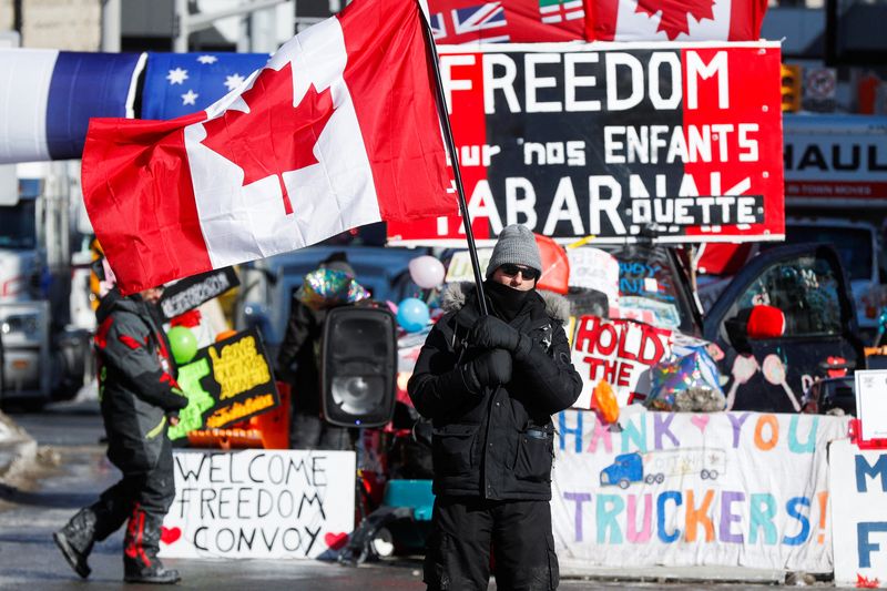 &copy; Reuters. A person waves a Canadian flag in front of banners in support of truckers, as truckers and supporters continue to protest the coronavirus disease (COVID-19) vaccine mandates, in Ottawa, Ontario, Canada, February 14, 2022. REUTERS/Lars Hagberg