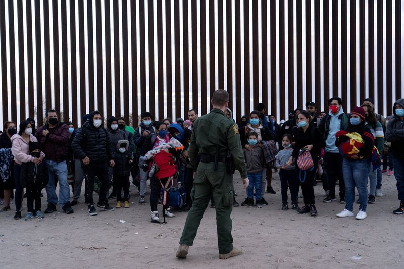 &copy; Reuters. Imagen de archivo de migrantes que buscan asilo en Estados Unidos de pie junto al muro fronterizo mientras esperan para ser procesados por la patrulla fronteriza de Estados Unidos después de cruzar la frontera desde México en Yuma, Arizona, Estados Unid