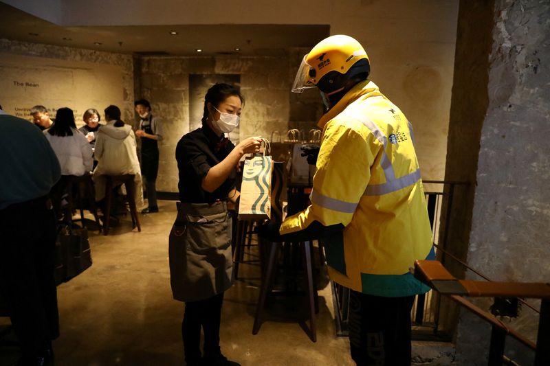 &copy; Reuters. FILE PHOTO - A staff member takes a bag of ordered food from a Meituan delivery worker during a media event of Starbucks launching a partnership with Meituan, at a Starbucks flagship store in Beijing, China January 18, 2022. REUTERS/Tingshu Wang