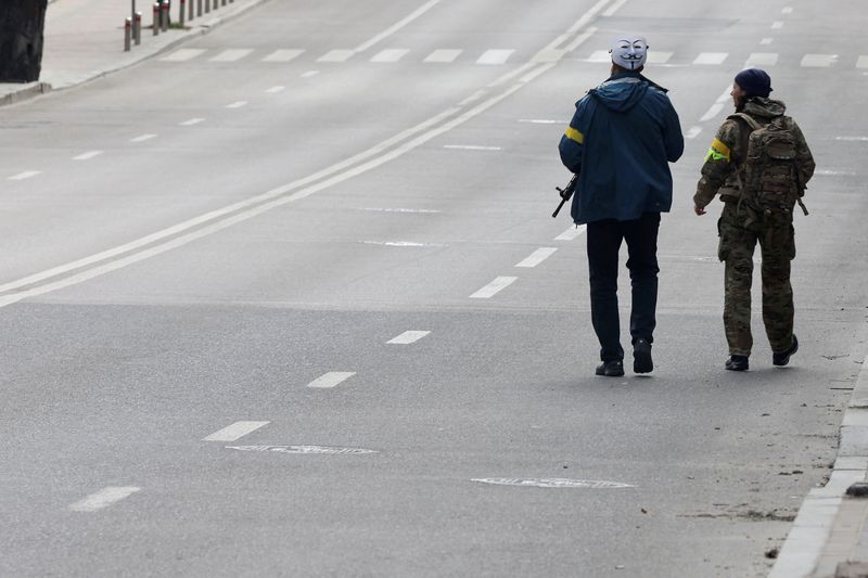© Reuters. فردان من قوات الدفاع الاقليمية عن الأراضي الأوكرانية يسيران في شارع يخلو من المارة خلال حظر التجول في كييف يوم الأحد. تصوير:كارلوس باريا-رويترز.