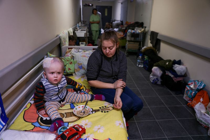 &copy; Reuters. Una mujer está sentada junto a un niño que está recibiendo tratamiento, en los pasillos del sótano del Hospital de Niños Okhmadet, en medio de la invasión de Rusia a Ucrania, en Kiev, Ucrania. 28 de febrero, 2022. REUTERS/Umit Bektas