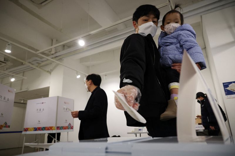 &copy; Reuters. A man holding his child casts his vote at a polling station during the presidential elections in Seoul, South Korea, March 9, 2022.  REUTERS/Kim Hong-Ji