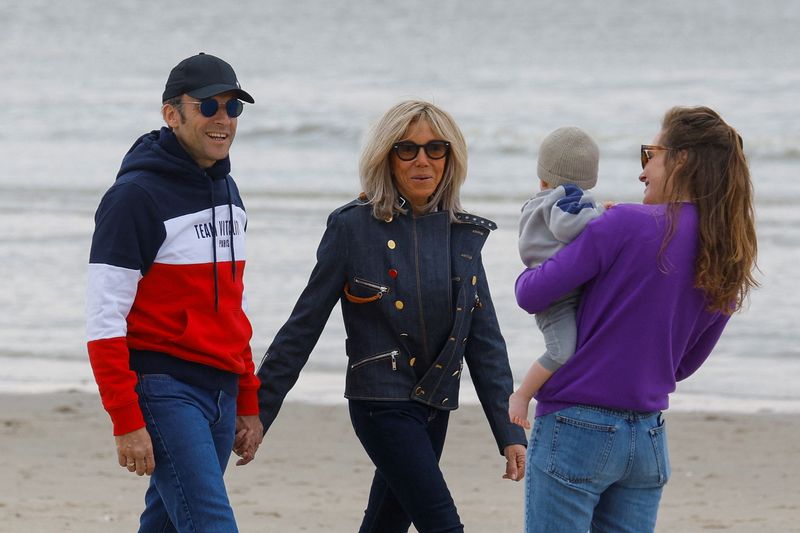 © Reuters. French President Emmanuel Macron, candidate for his re-election in the 2022 French presidential election, and his wife Brigitte Macron greet people as they walk on the beach, on the eve of the second round of the presidential election, in Le Touquet-Paris-Plage, France, April 23, 2022. REUTERS/Gonzalo Fuentes