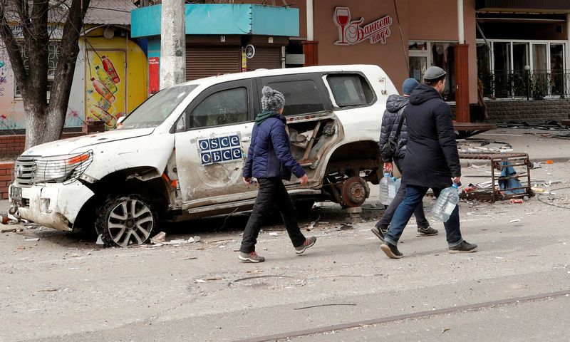 &copy; Reuters. Imagen de archivo de gente pasando junto a un auto dañado de la OSCE en Mariúpol, Ucrania. 1 abril 2022. REUTERS/Alexander Ermochenko