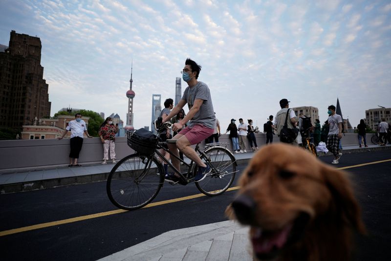 © Reuters. A man wearing a protective face mask cycles past people and a dog on a bridge, as the city prepares to end the lockdown placed to curb the coronavirus disease (COVID-19) outbreak in Shanghai, China May 31, 2022. REUTERS/Aly Song