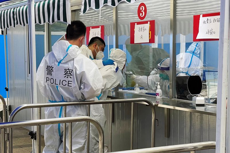 &copy; Reuters.  ６月２日、中国国家衛生健康委員会は新型コロナウイルスの核酸検査の監視を強化すると発表した。写真は１日、ロックダウンが解除された上海で、男性を検査施設に連れてきた警察官ら