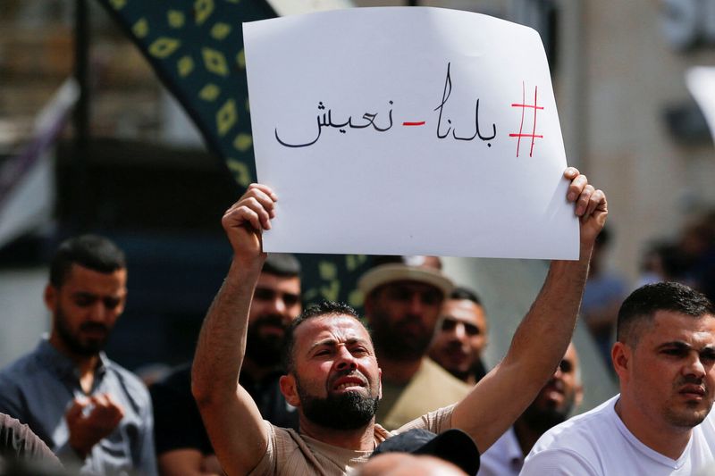 &copy; Reuters. فلسطيني يحمل لافتة مكتوب عليها "بدنا نعيش" خلال احتجاجات على ارتفاع الأسعار  في الخليل في الضفة الغربية يوم الأحد. تصوير: موسى قواسمة - رويترز
