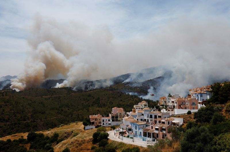 &copy; Reuters. Un helicóptero vuela antes de hacer una descarga de agua mientras el humo de un incendio forestal ondea cerca de las casas en Benahavís, España. 9 de junio de 2022. REUTERS/Jon Nazca