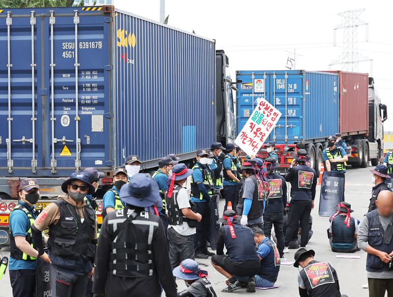 © Reuters. Trucks transporting containers drive past members of the Cargo Truckers Solidarity union gathering in front of an inland containers depot in Uiwang, South Korea, June 13, 2022.   Yonhap via REUTERS   