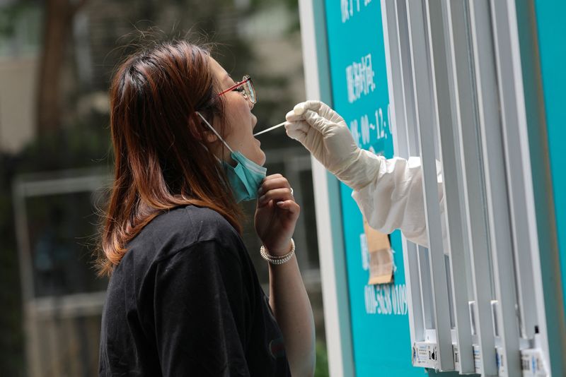 © Reuters. عامل طبي يأخذ عينة مسحة من إحدى السيدات في كشك متنقل لاختبار الحمض النووي يوم الاثنين مع تفشي وباء كوفيد-19 في بكين. تصوير: تينجشو وانغ - رويترز 