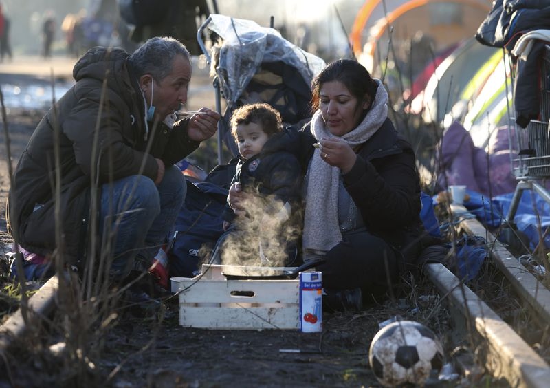 &copy; Reuters. Des migrants mangent en attendant dans un camp de migrants improvisé à Dunkerque, près de Calais. Alors qu'un premier vol à destination de Kigali a été bloqué cette semaine par une décision de la Cour européenne des droits de l'homme, provoquant 