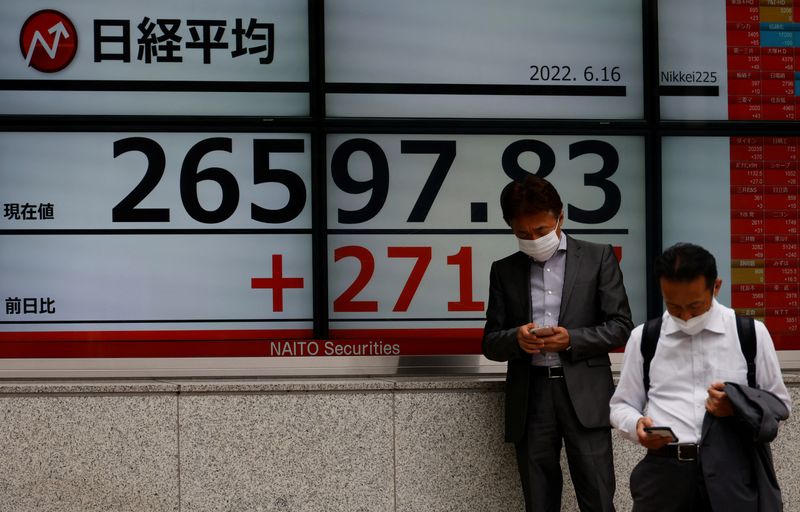 &copy; Reuters. FILE PHOTO: Men wearing protective masks amid the coronavirus disease (COVID-19) outbreak, use mobile phones in front of an electronic board displaying Japan's Nikkei index outside a brokerage in Tokyo, Japan June 16, 2022. REUTERS/Kim Kyung-Hoon