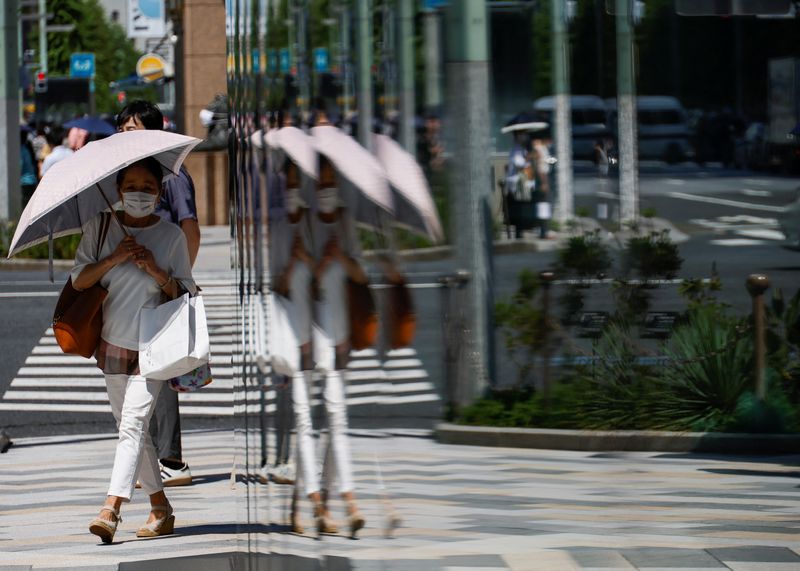 © Reuters. FILE PHOTO: A woman holding an umbrella is reflected on a window while walking along a street, as the Japanese government issues a warning over a possible power crunch due to a heatwave in Tokyo, Japan June 28, 2022.  REUTERS/Issei Kato