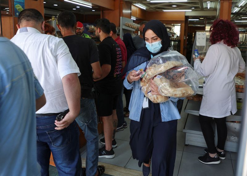 &copy; Reuters. أشخاص يقفون في طابور وامرأة تحمل الخبز في أحد مخابز بيروت يوم الاربعاء. تصوير: محمد عزاقير - رويترز. 