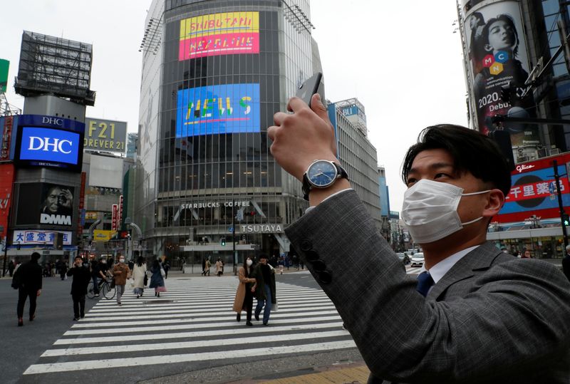 &copy; Reuters. FILE PHOTO: A man wearing a protective face mask, takes a photo with his mobile phone at noon, at Shibuya Crossing, during the coronavirus disease (COVID-19) outbreak, in Tokyo, Japan, March 31, 2020. REUTERS/Issei Kato  