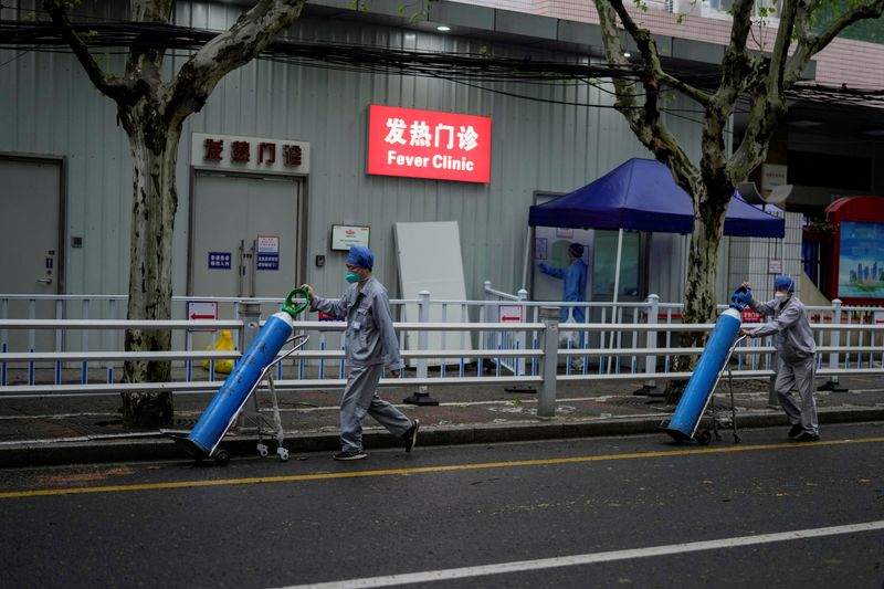 &copy; Reuters. عاملان ينقلان اسطوانات الأكسجين خارج عيادة الحمى بأحد المستشفيات أثناء الإغلاق وسط تفشي جائحة فيروس كورونا في شنغهاي بالصين يوم 14 أبريل ني